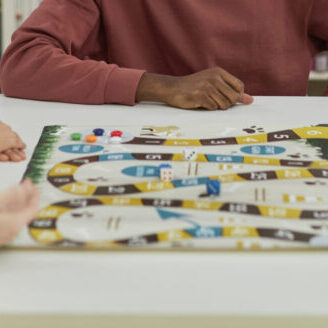 Diverse group of young people playing board games together while sitting around table in library and smiling
