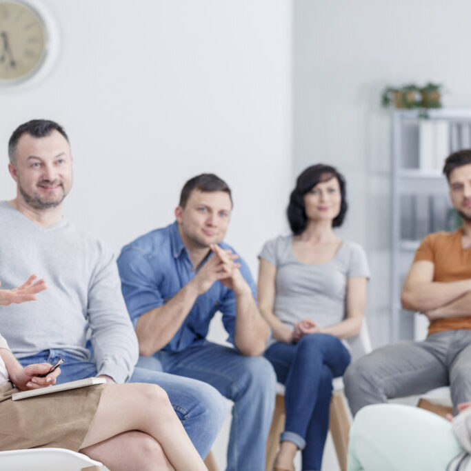 Therapist congratulating young woman on her progress in therapy and happy family blurry in the background